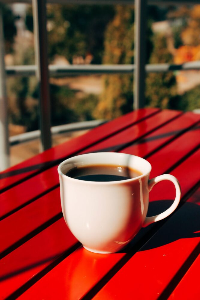 Hvid kaffekop på et rødt cafébord i sollys