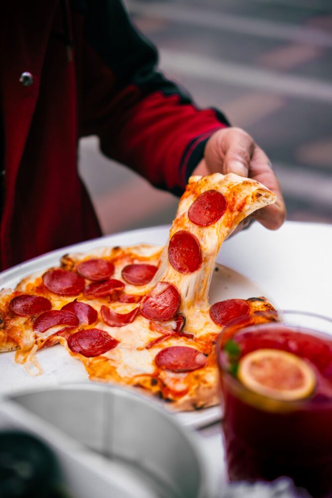 En hånd løfter et stykke pepperonipizza med smeltet ost
