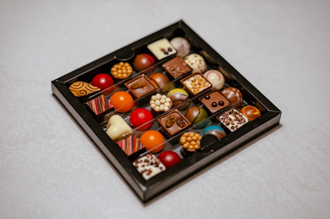 Æske med fyldte chokolader i forskellige farver på et lyst bord