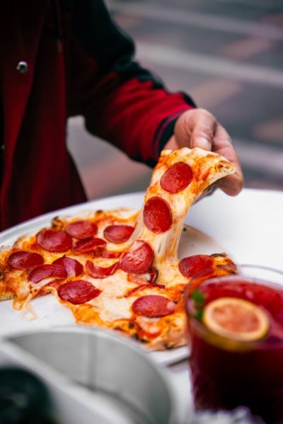 En hånd løfter et stykke pepperonipizza med smeltet ost