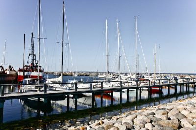 Lystbåde og bådebroer i Hornbæk Havn under en blå himmel
