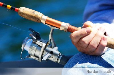 Hænder holder en fiskestang med fiskehjul