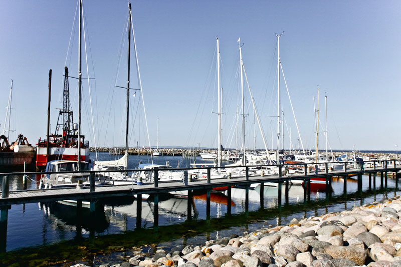 Lystbåde og bådebroer i Hornbæk Havn under en blå himmel