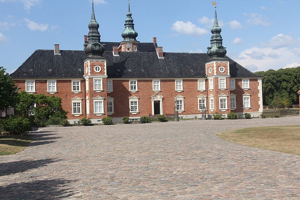 Jægerspris Slots røde facade og tre tårne under blå sommerhimmel