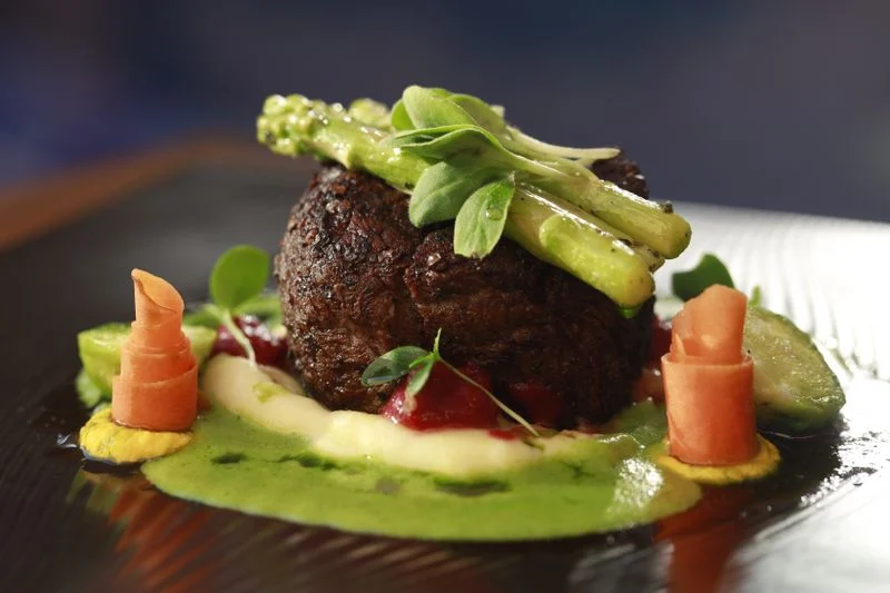 Kød anrettet med grøntsager og sauce på en tallerken