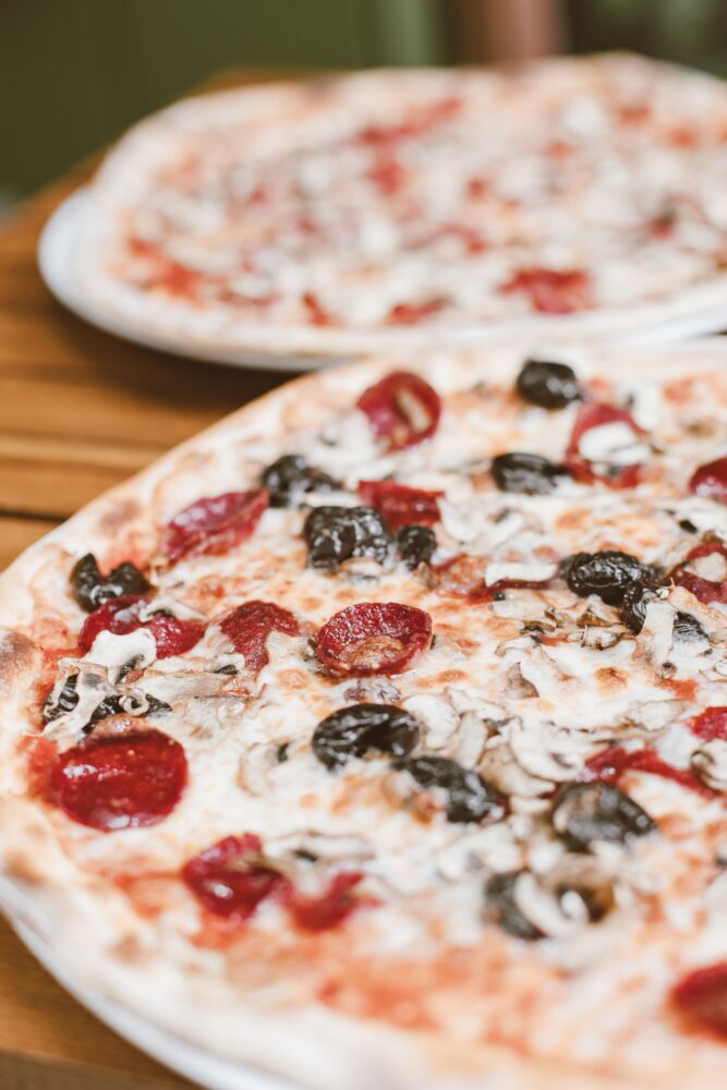 To pizzaer med oliven, svampe og pepperoni på et træbord