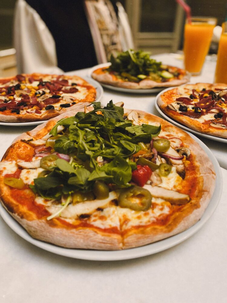 Flere pizzaer med friske grøntsager og grønne blade på bordet
